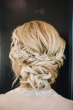 a woman with blonde hair wearing a braided updo and some flowers in her hair