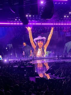 a woman standing on top of a stage with her arms in the air and hands up