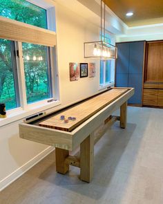 a pool table in the middle of a room with two windows and lights hanging from the ceiling