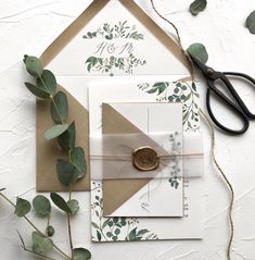 the wedding stationery is laid out on top of the table with scissors and greenery