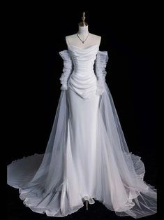 a white wedding dress with long sleeves and a veil on display in front of a black background