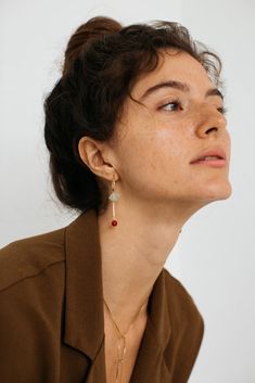 a woman wearing a brown shirt and gold necklace with red beads on her left ear