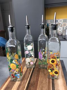 three glass bottles with flowers painted on them sitting on a wooden table in a kitchen