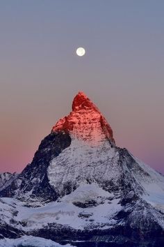 the moon is setting on top of a snowy mountain