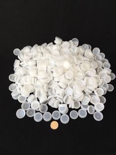 a pile of white plastic cups sitting on top of a black table next to a gold coin