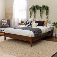 a bed with pillows and plants on the headboard is in a room that has hardwood floors