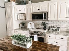 a kitchen with white cabinets and wood counter tops, an island in the middle has plants on it