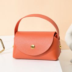 an orange handbag sitting on top of a white table next to a pair of glasses