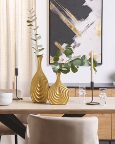 two gold vases sitting on top of a wooden table in front of a painting