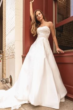 a woman in a white wedding dress leaning against a red door and posing for the camera