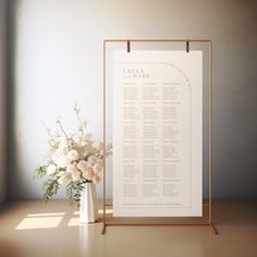 a white and gold wedding seating chart next to a vase with flowers on the table