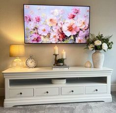 a white entertainment center with flowers on the wall and candles in vases next to it