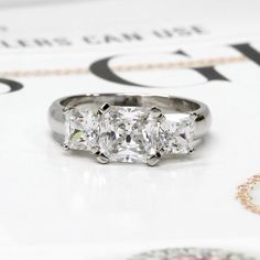 three stone diamond ring sitting on top of a magazine