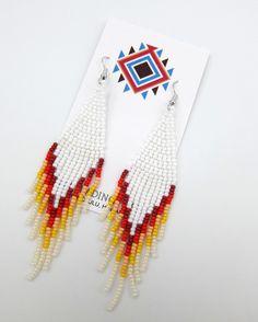 a pair of beaded earrings with red, yellow and white beads hanging from it