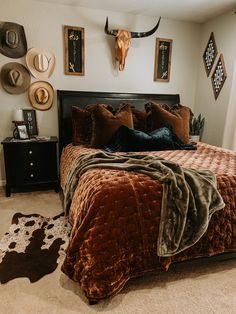 a bed with brown and black comforter in a bedroom next to a cow skull on the wall