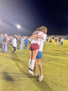 two people embracing each other on a soccer field at night with spectators in the background