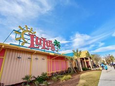 the entrance to an amusement park with people walking by and palm trees in the background