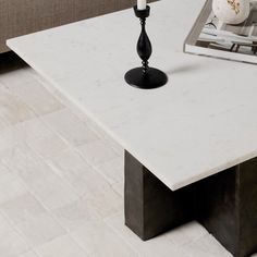 a white marble coffee table with a black candle holder on it's end, in front of a couch