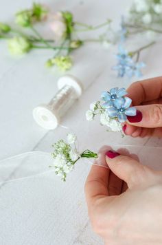 two hands are holding small flowers on a white table with some sewing thread and spools