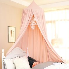 a bed with a pink canopy over it and pillows on the bottom side, in front of a window