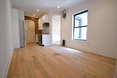 an empty living room with hard wood flooring and white walls in the background is a kitchen