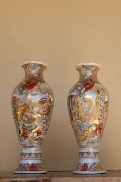 two large vases sitting on top of a wooden shelf in front of a wall