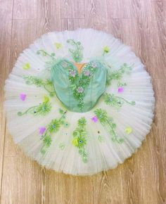 a white tutu with green and pink flowers on it's bottom, sitting on a wooden floor