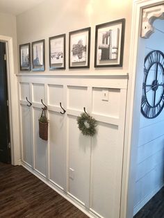 a clock mounted to the side of a wall next to pictures and wreaths on hooks