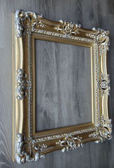 an ornate gold frame hanging on the wall with wood paneling in the back ground