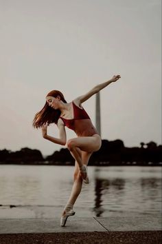 a woman in a red and white bathing suit is doing a ballet move by the water