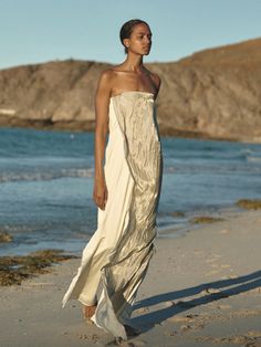 a woman standing on top of a sandy beach next to the ocean wearing a white dress