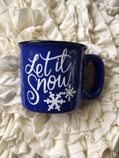 a blue coffee mug with let it snow written on it sitting on a white flower