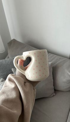 a stuffed animal holding a coffee cup on its head in front of a gray couch