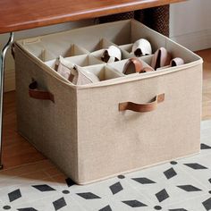 an open canvas storage box on the floor with shoes in it next to a wooden table