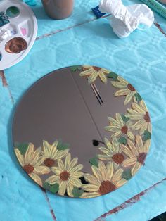 a mirror with sunflowers painted on it sitting on a table next to paintbrushes