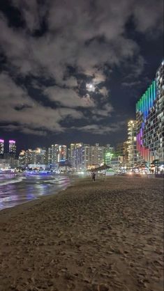 the city lights shine brightly in the night sky as people walk on the beach near the water