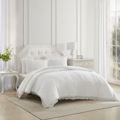 a white bed in a bedroom next to a window