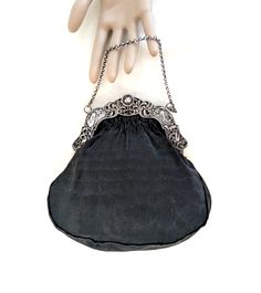 A black handbag with a Dutch 2nd standard silver (.833 purity), repousse frame with windmills, birds, a baby's face, and a cable chain handle.  The interior of the bag is hand sewn, taupe thick gauge, silk satin, and it has two small, side pockets.  The exterior silk is a finely ribbed matte black silk.  The handle drop is 3 1/2 inches, its overall dimensions are 7 1/2 H x 7 1/2 W x 1/2 D inches.  The bag dates from the late 19th to the first half of the 20th century. CONDITION:  Some signs of w Silver Handheld Evening Bag With Chain Strap, Handheld Silver Evening Bag With Chain Strap, Silver Shoulder Bag With Palladium Hardware For Evening, Silver Formal Bag With Chain Strap, Silver Clutch Shoulder Bag With Dust Bag, Silver Clutch Shoulder Bag With Dust Bag Included, Elegant Silver Bag With Chain Strap, Classic Silver Shoulder Bag With Chain Strap, Antique Style Evening Clutch Bag