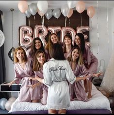 a group of women in pink robes standing on top of a bed next to balloons