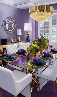 a dining room with purple walls and gold trim around the table, white chairs and chandelier