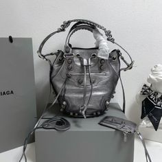 Balenciaga 's popular 'Le Cagole' series is a modern interpretation of its 'City' handbags - reshaped into a bucket bag design to inject a new soul into it. The large size adds two round top handles, combining classic and Modern trends are perfectly integrated. On the basis of retaining the original DNA of the motorcycle bag's flat rivets, delicate buckles and tassel zippers, it adds adjustable woven shoulder straps and a cute and playful heart-shaped mirror, which perfectly softens the neutral Designer Bucket Bag With Detachable Strap, Designer Top Handle Bucket Bag For Shopping, Designer Bucket Bag For Daily Use, Designer Large Capacity Bucket Bag For Shopping, High-end Bucket Bag With Removable Pouch, High-end Bucket Satchel, High-end Bucket Satchel With Detachable Handle, Designer Bucket Bag With Detachable Handle, Designer Tote Bucket Bag With Detachable Handle