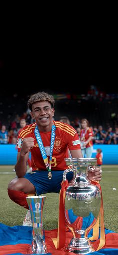 a man kneeling down next to a silver trophy on top of a field with people in the background