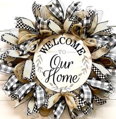 a welcome to our home wreath hanging on the wall with black and white checkered ribbon