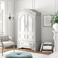 a white armoire in a living room next to a chair and ottoman on a rug