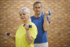 an older couple exercising with dumbbells in front of a brick wall