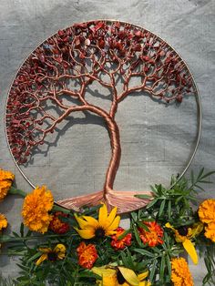 a metal tree with yellow and red flowers around it