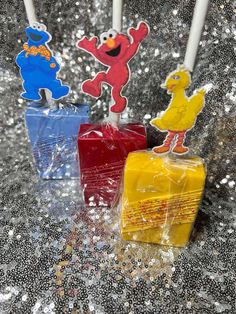 three candles with sesame street characters on them sitting in front of silver sequins