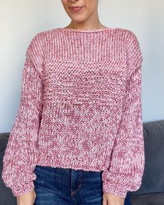 a woman standing in front of a couch wearing a pink sweater