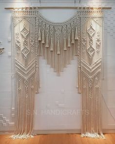 a white wall hanging on the side of a wooden floor next to a window with tassels