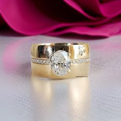 a close up of a wedding ring with a diamond on it and a pink rose in the background